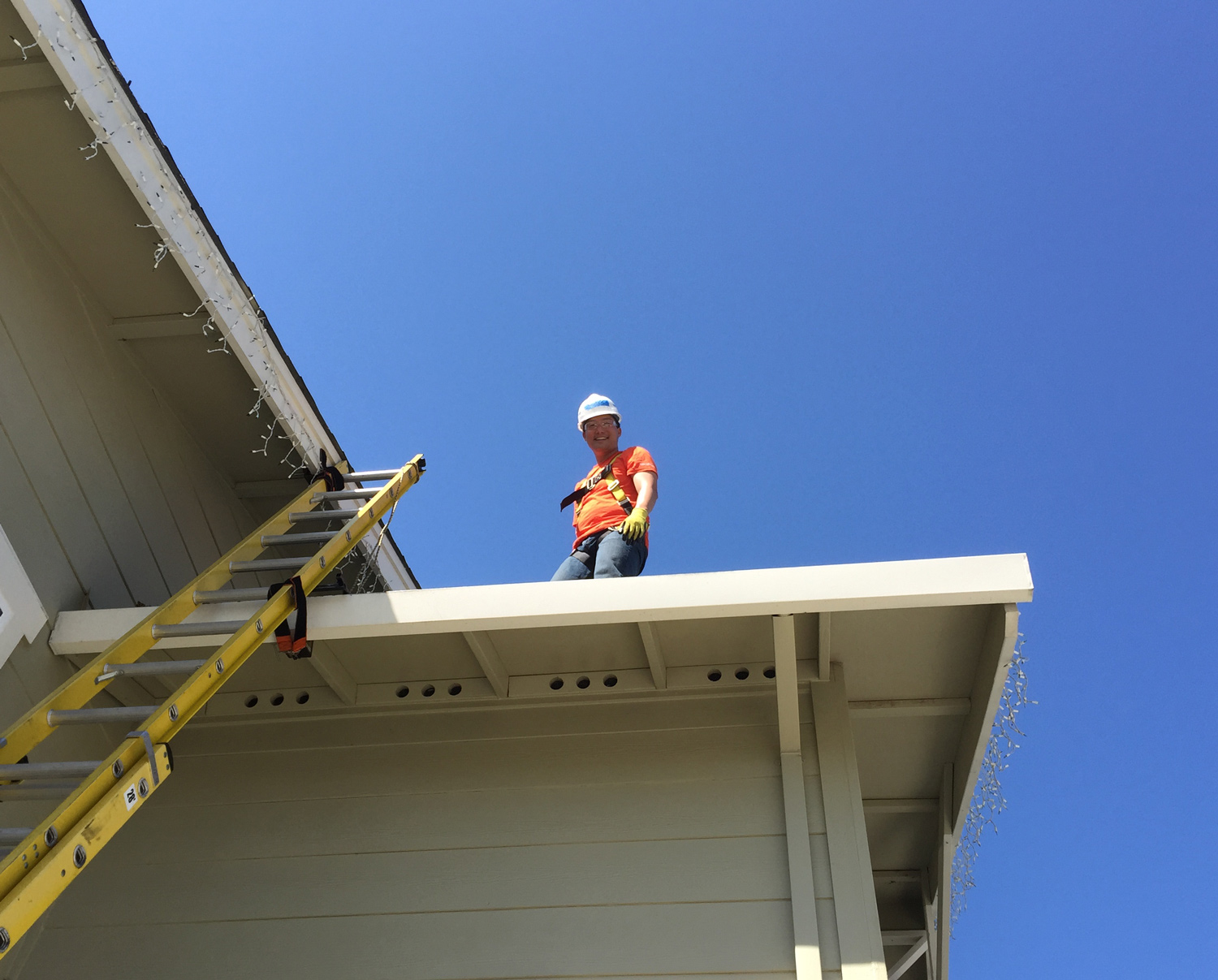 Thomas Lee on the roof of a house, wearing a construction helmet and vest